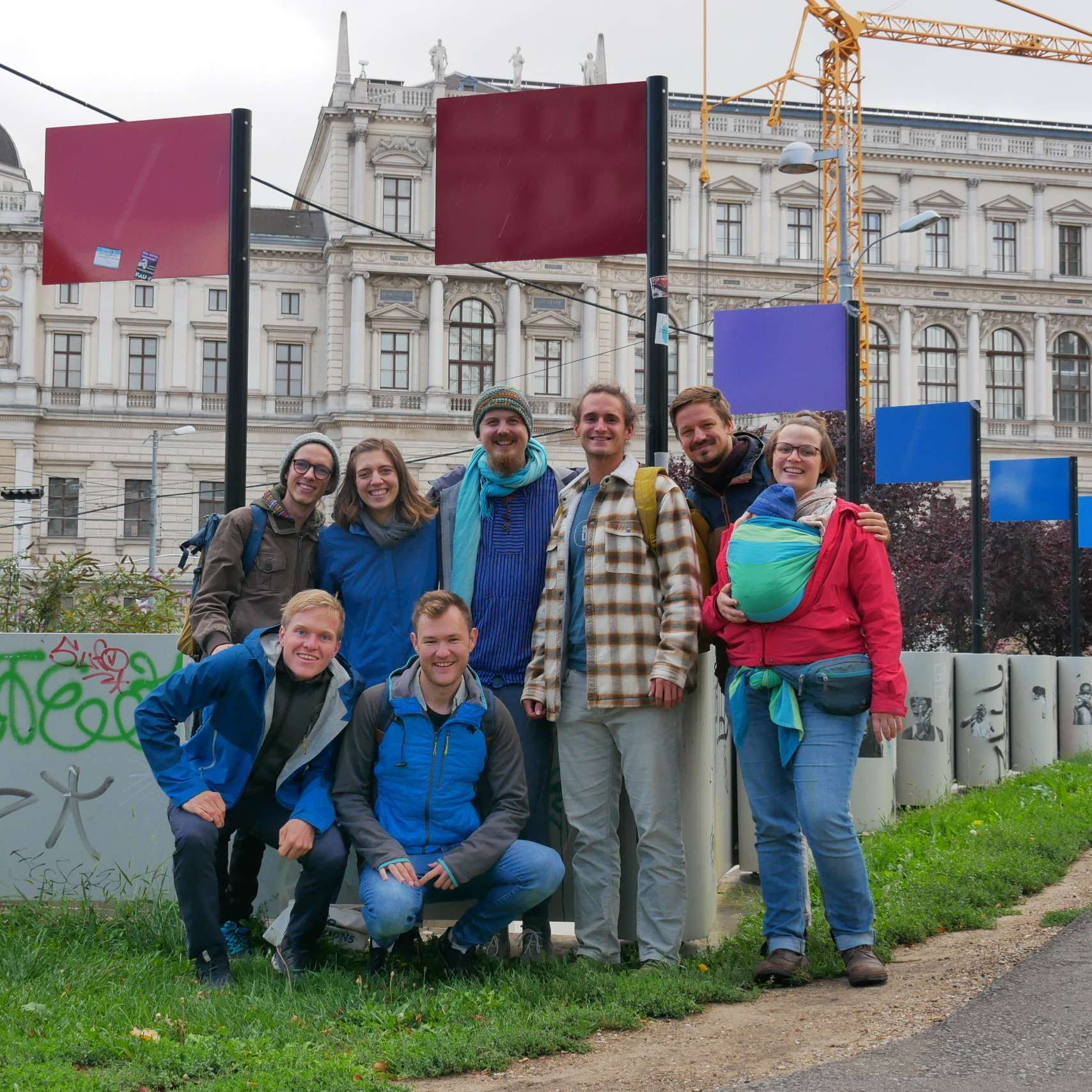 Group of joyful people posing outdoors with historic building backdrop, showcasing travel and tourism in an urban setting.